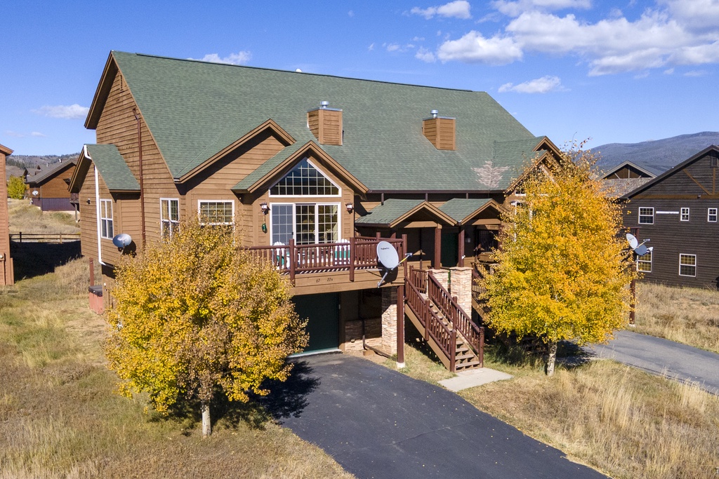 Mountain lodge with warm wood siding and green roof nestled among golden autumn trees in a peaceful residential setting.
