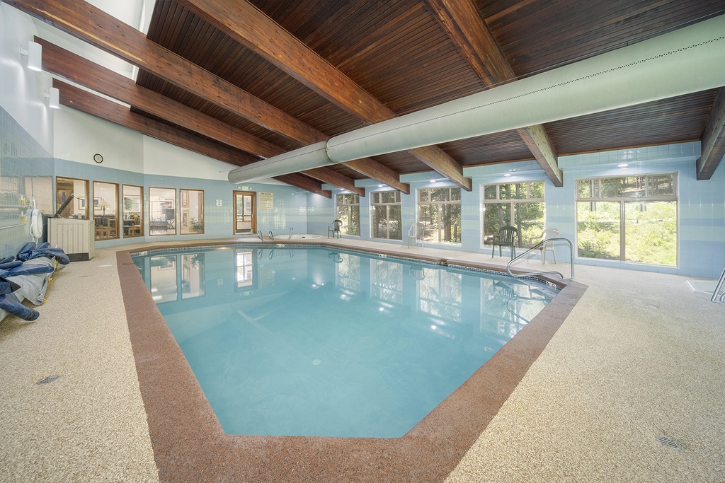 Dive into the clubhouse indoor pool beneath stunning exposed wood beams, where natural light pours through windows overlooking the surrounding trees and greenery.