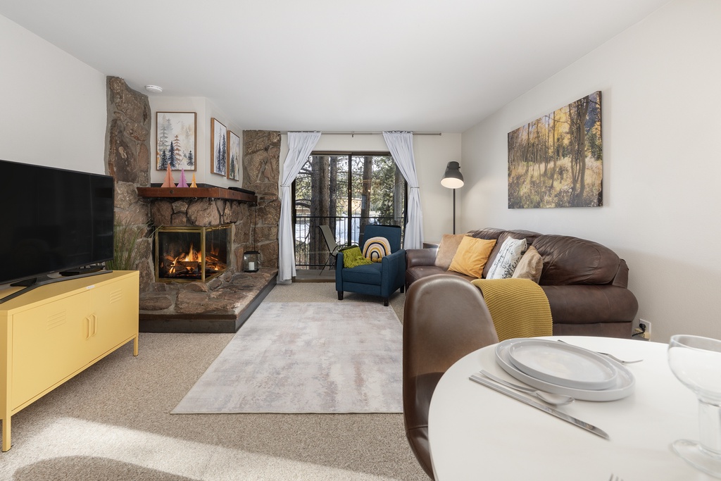 Unwind in your cozy living space with a crackling stone fireplace, plush leather sofa, and peaceful forest views from your private balcony.