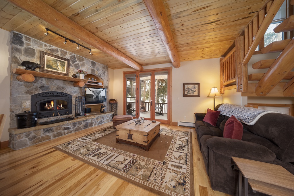 Cozy up in this inviting living room with crackling stone fireplace, exposed beams, and warm lighting perfect for your mountain retreat.