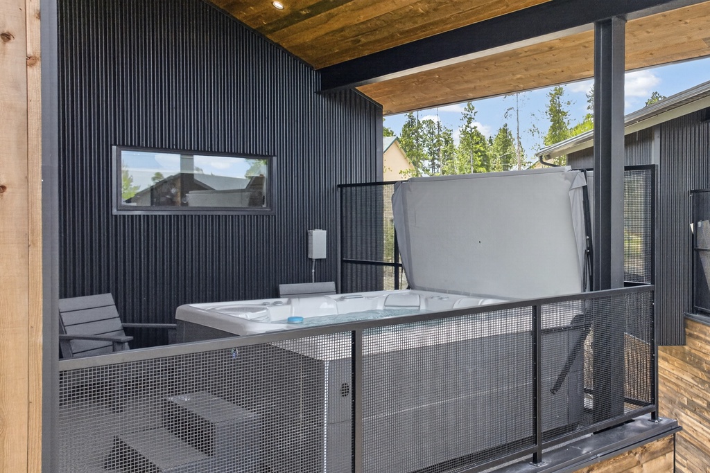 The property features a private outdoor hot tub area with modern corrugated metal walls and natural wood ceiling. A secluded space for relaxing under the trees.
