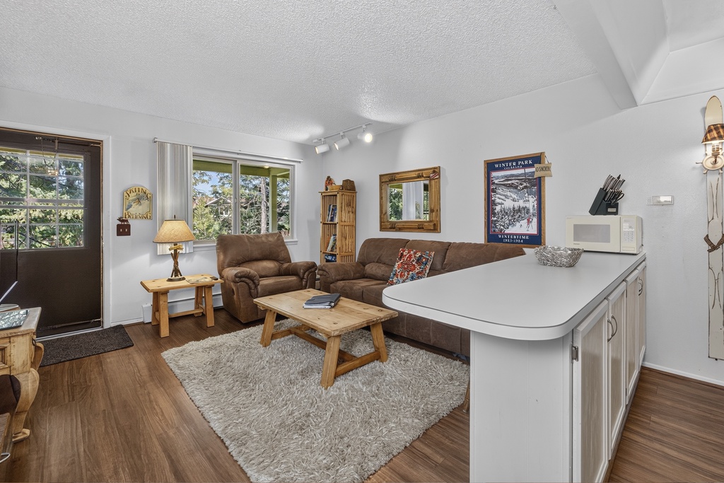 Step into your comfortable mountain retreat where warm wood tones and cozy furnishings welcome you home. Natural light pours through large windows framing tree-lined views, inviting you to relax in this inviting space.