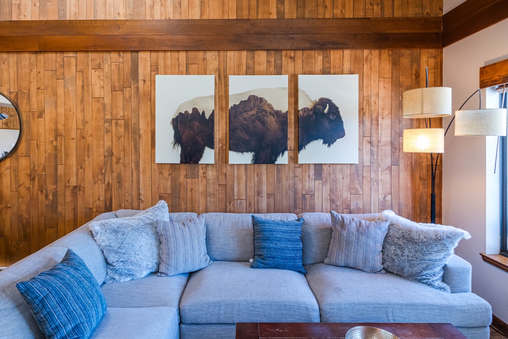 Sink into this plush sofa surrounded by warm wood walls and striking buffalo art—your perfect spot to unwind after mountain adventures.