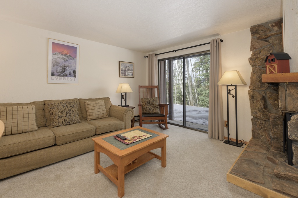 Unwind in your cozy living room with a crackling stone fireplace and private patio access to snowy surroundings.