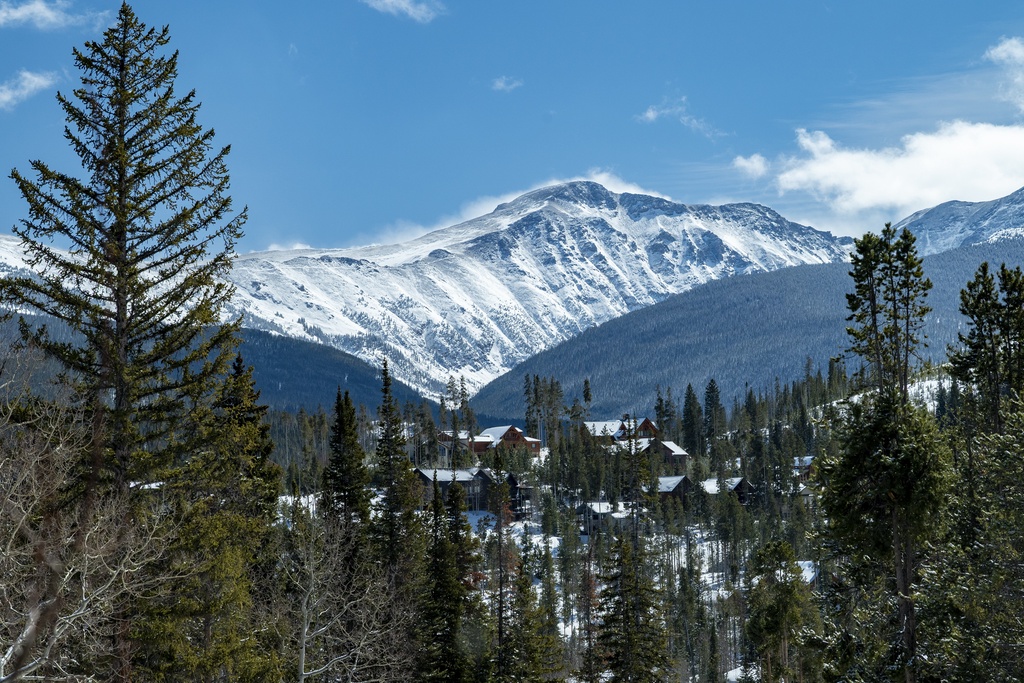 Stunning mountain landscape with snow-capped peaks rising above a forested valley dotted with cozy cabins.