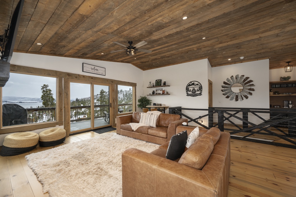 Unwind in your rustic-elegant living room featuring warm leather seating, exposed wood beams, and expansive windows showcasing stunning lake views.