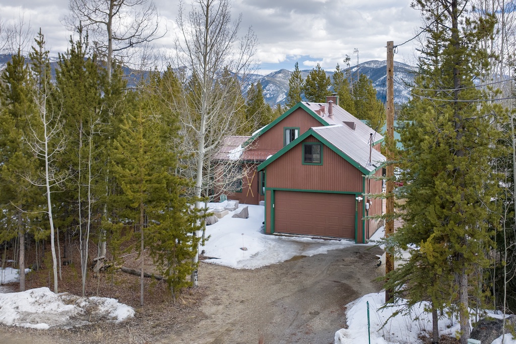 Mountain cabin with green trim nestled among evergreens and snow-covered landscape, offering scenic wilderness access.