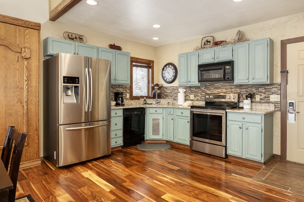 Step into your fully-equipped kitchen at Mountainside Unit B-8 with gleaming hardwood floors, modern stainless steel appliances, and charming turquoise cabinets that make cooking feel like home.