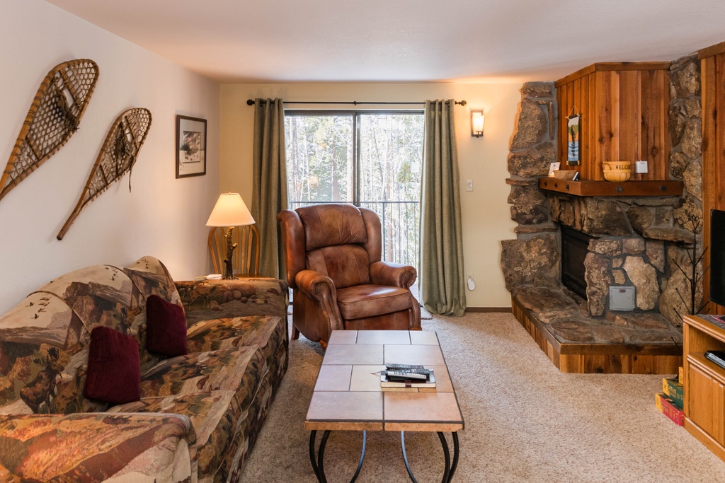 Cozy up by your stone fireplace with woodland views through large windows, perfect for relaxing evenings.