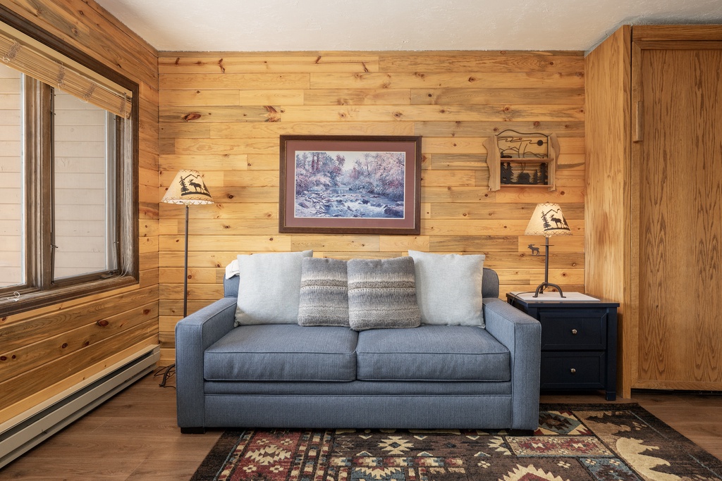 Sink into rustic charm with your cozy gray sofa surrounded by warm knotty pine walls and thoughtful mountain décor.