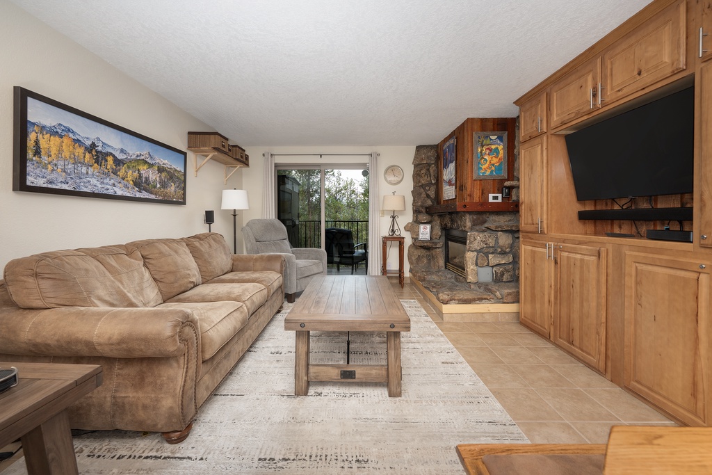 Cozy living room with stone fireplace and mountain views through glass doors creates your perfect mountain retreat atmosphere.