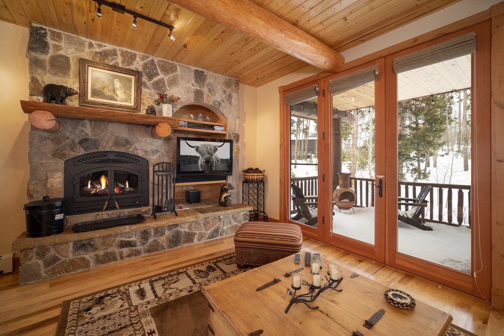 Cozy up by your crackling stone fireplace while snowy mountain views frame your perfect winter retreat through expansive glass doors.