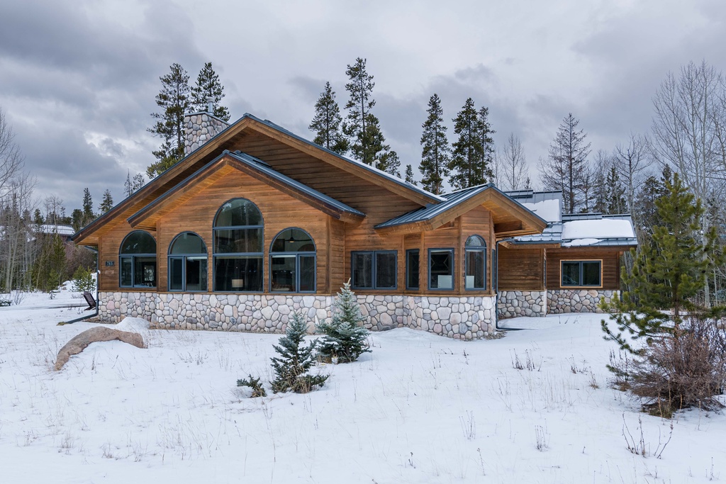 Stunning log and stone property nestled among towering pines in a pristine winter wonderland setting.
