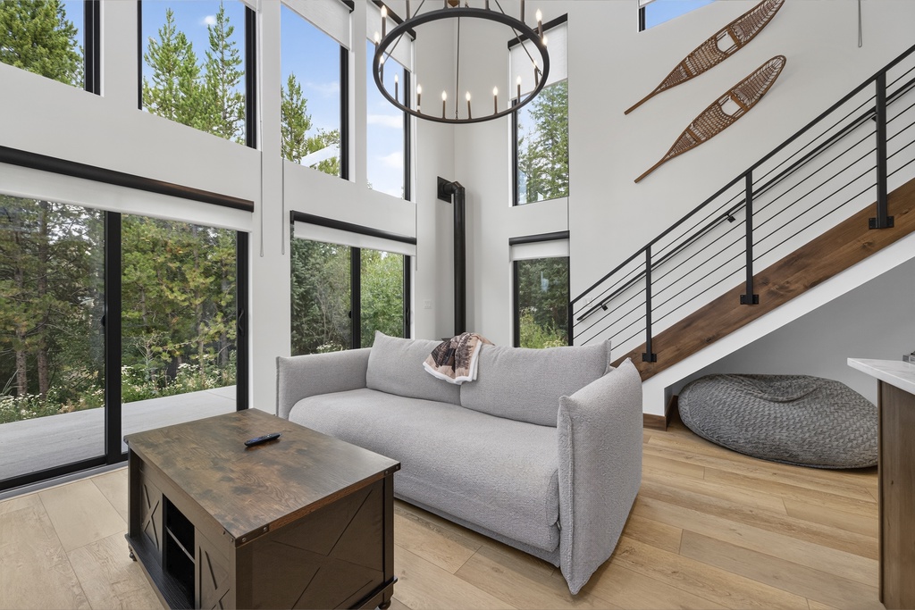Soaring ceilings and floor-to-ceiling windows frame your peaceful forest view, while the cozy seating area invites you to unwind beneath a statement chandelier in this bright, airy living space.