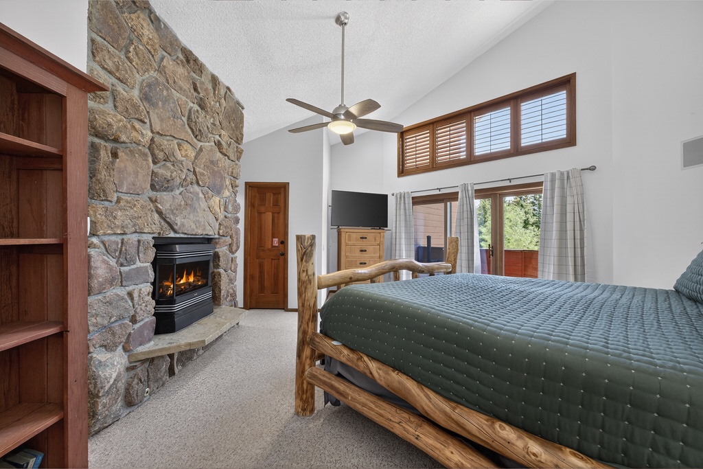 Unwind in your cozy mountain retreat with a roaring stone fireplace, rustic log-framed bed, and peaceful views. High ceilings and natural light create the perfect escape for restful nights.