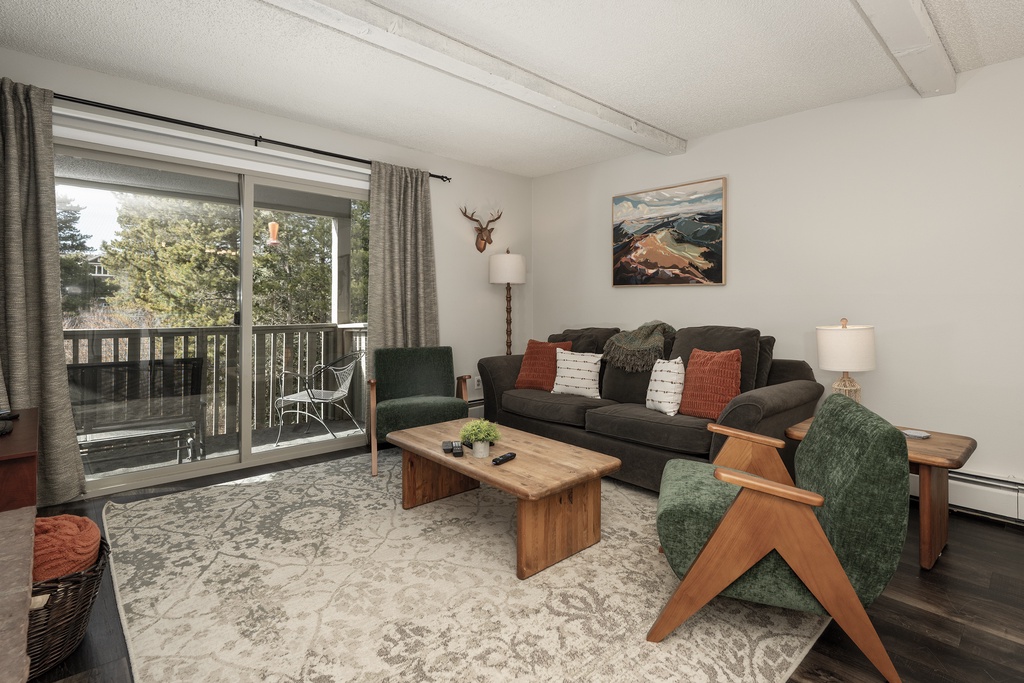 Relax in your cozy living room with rustic charm, featuring a plush sofa and warm wood accents overlooking peaceful treetops from your private balcony.