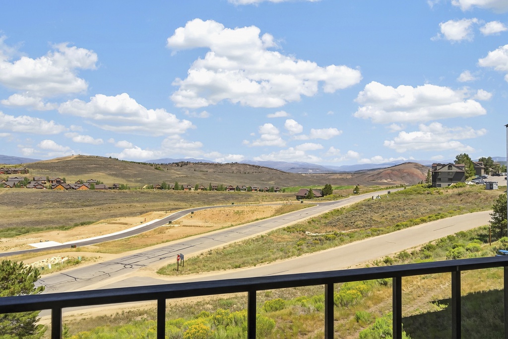 This property offers a scenic overlook of the surrounding neighborhood, with rolling hills and open landscapes stretching into the distance under a bright, expansive sky.