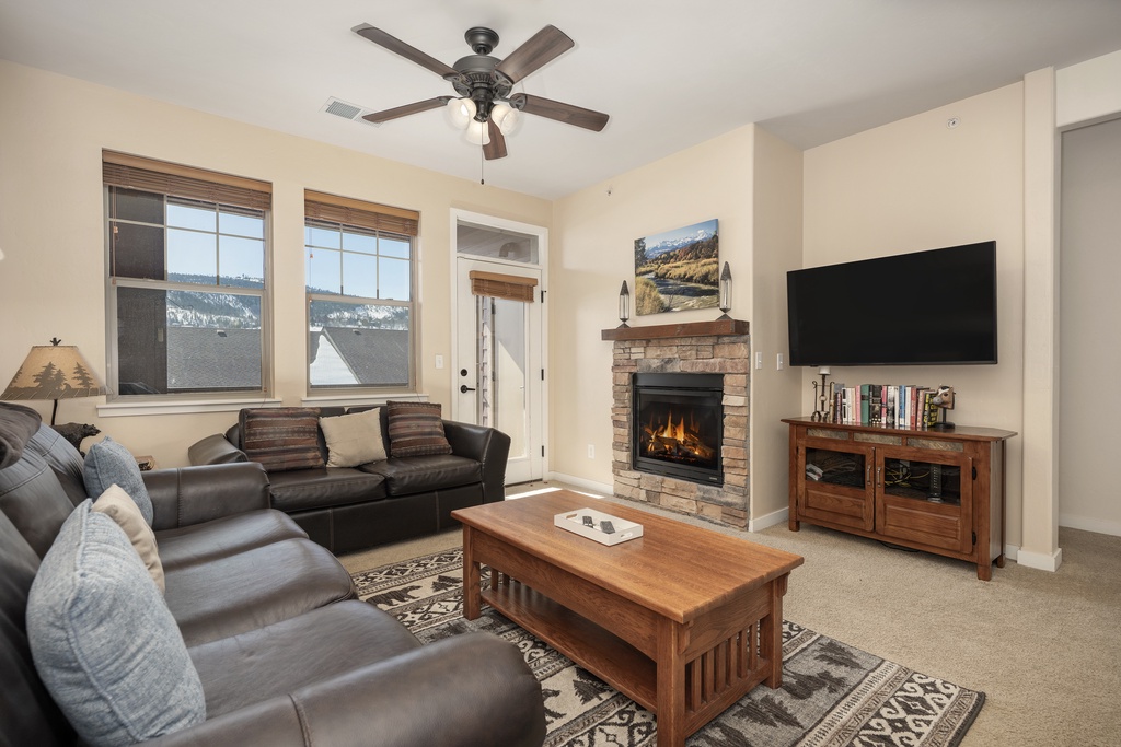 Cozy up in your inviting living space with a crackling fireplace, plush seating, and mountain views through large windows.