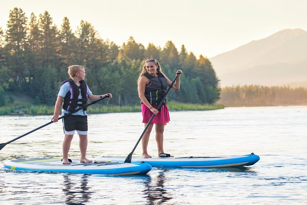 Paddleboard adventure on pristine mountain lake during your stay at Soda Springs Ranch condo 3C, surrounded by peaceful forest and distant peaks.