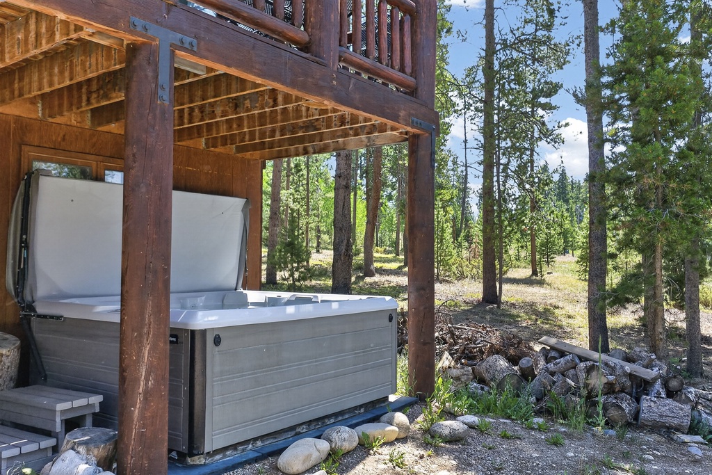 A peaceful mountain retreat surrounded by tall pines and natural landscape, featuring a private hot tub sheltered beneath a wooden deck for relaxation after exploring the wilderness.
