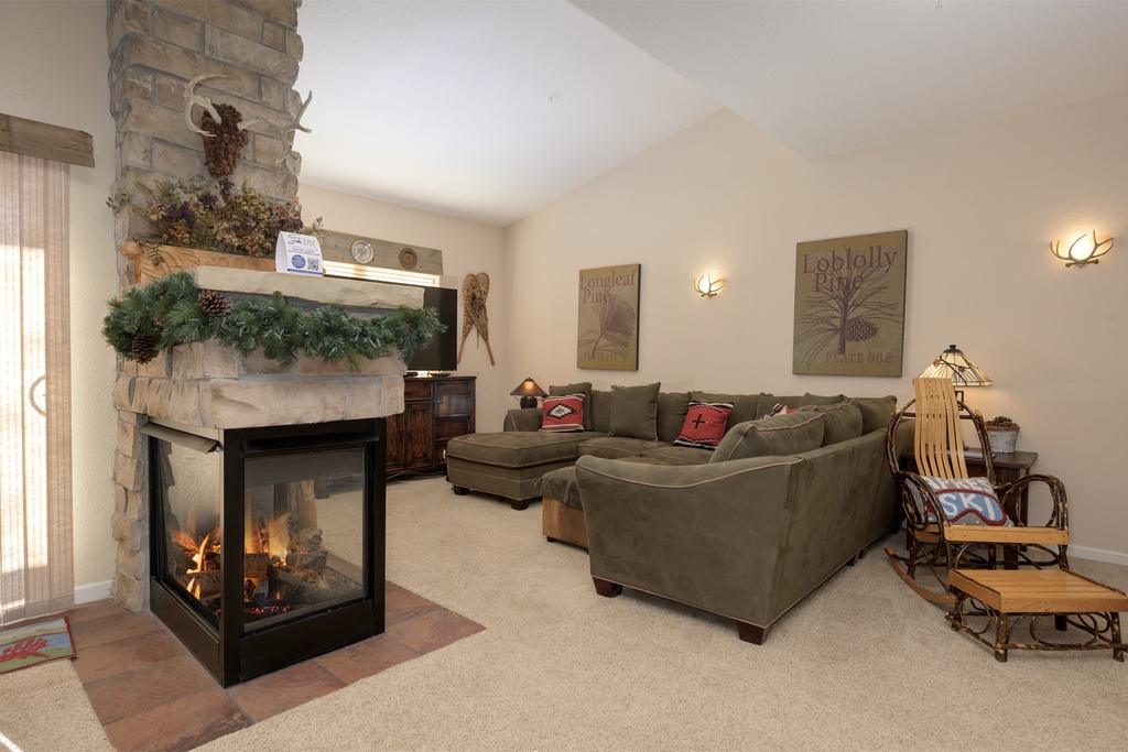 Gather around the cozy stone fireplace with plush sectional seating, where warm flames and comfortable furnishings create your perfect mountain retreat.