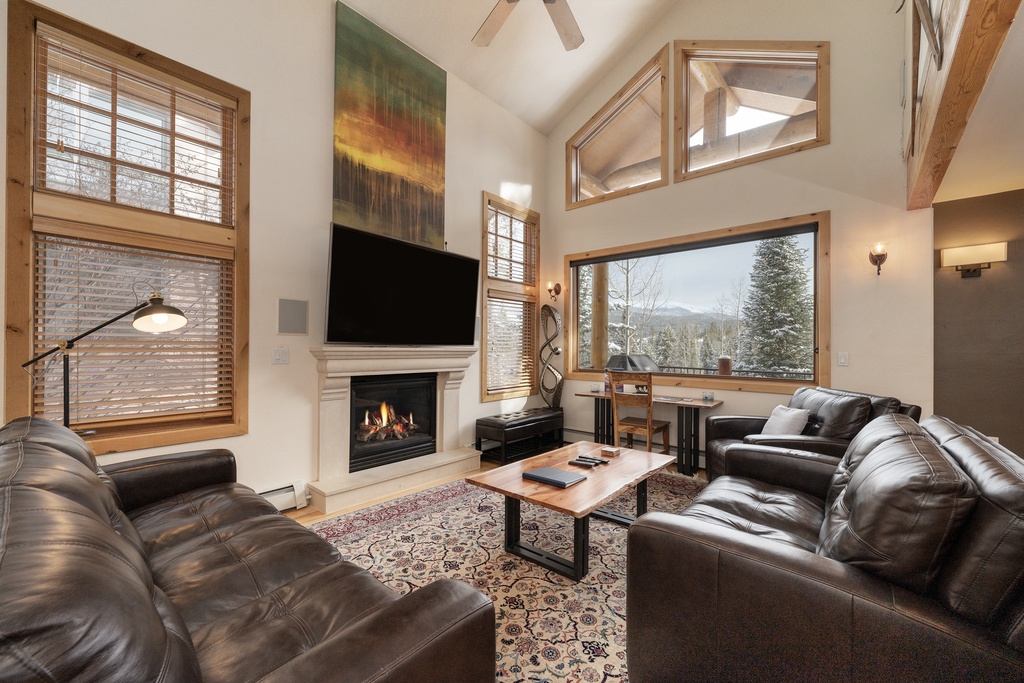 Cozy up in your spacious living room with leather seating, crackling fireplace, and stunning mountain views through floor-to-ceiling windows.
