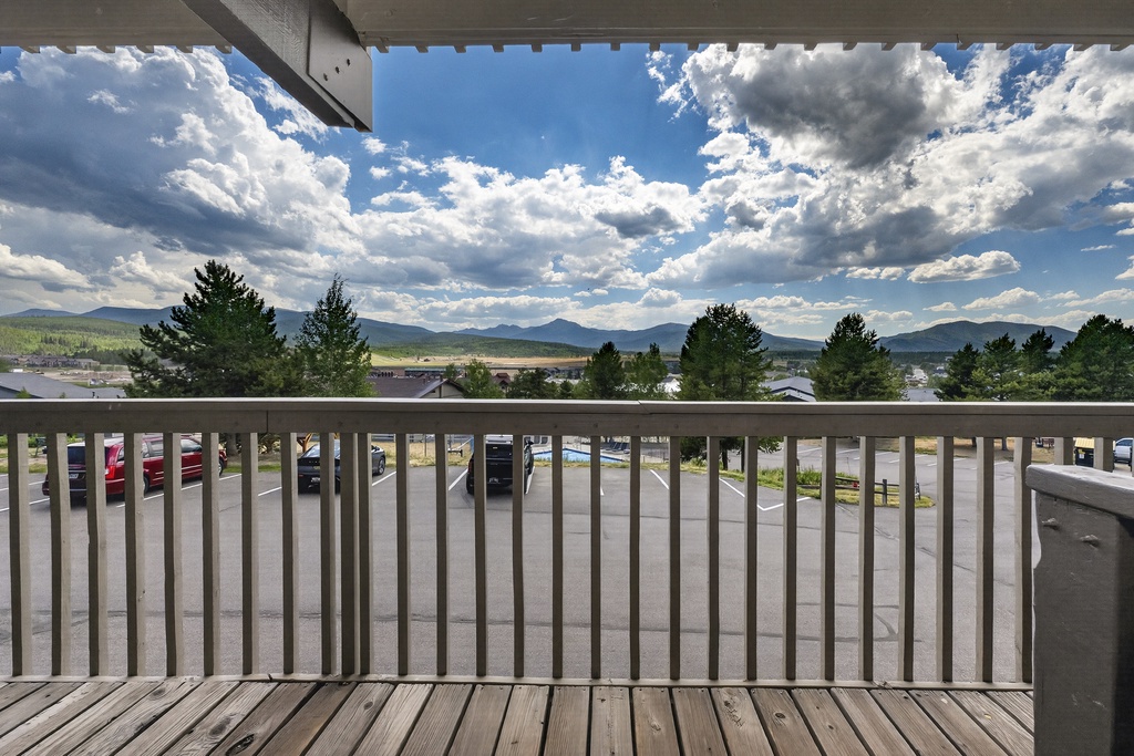 A balcony view capturing mountain ranges and expansive sky, with parking and local surroundings visible below—part of the area surrounding your arrival.