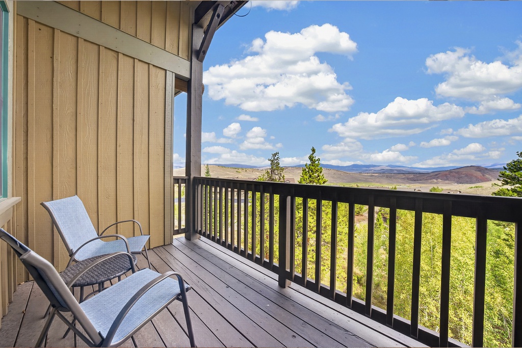 Sweeping views of rolling hills and open skies stretch before a private balcony, where comfortable chairs invite you to relax and soak in the quiet beauty of the surrounding landscape.
