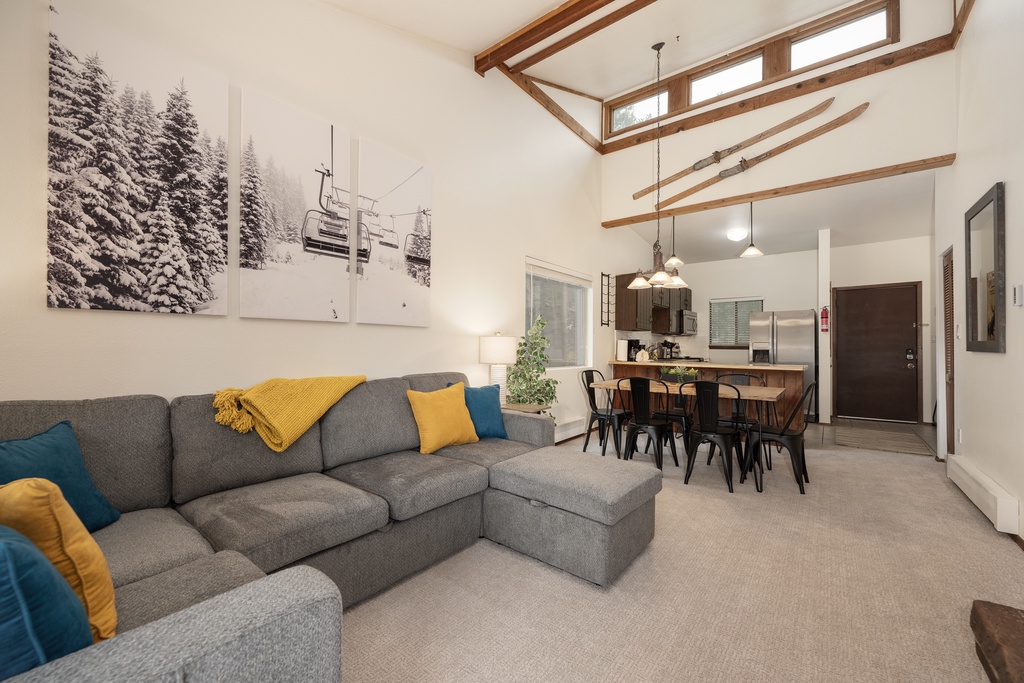 Relax in your open-concept living space with soaring wood beam ceilings and cozy sectional seating, perfect for unwinding after mountain adventures.