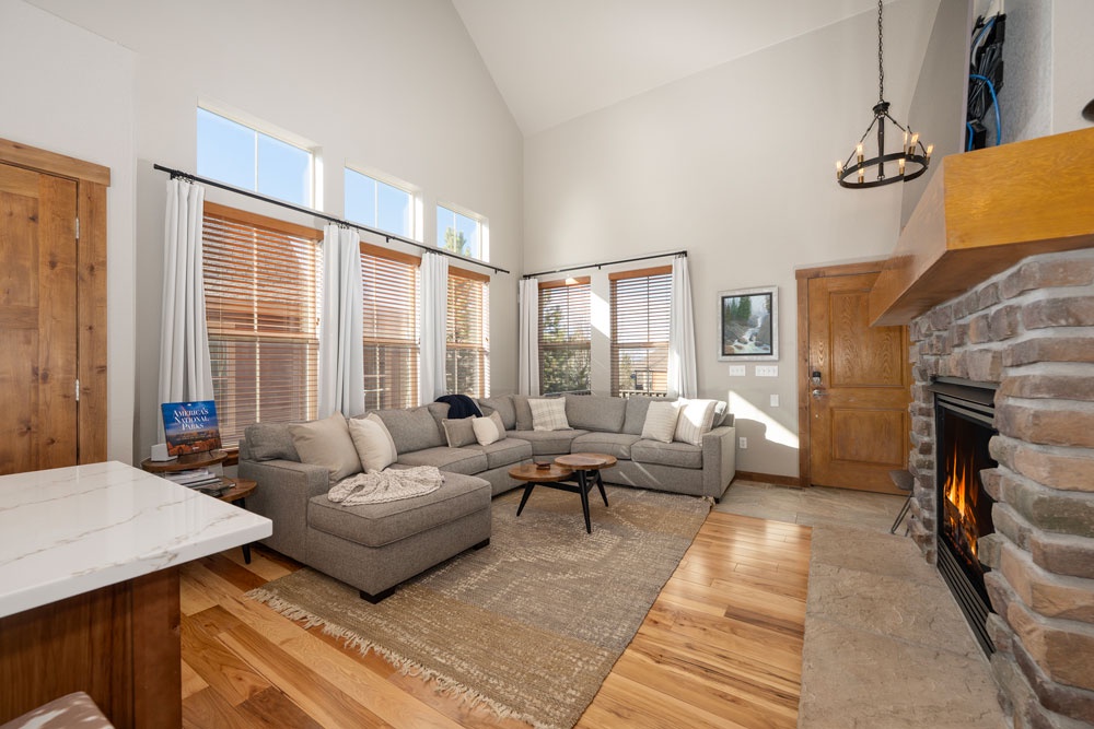 Relax in your spacious living room featuring vaulted ceilings, cozy stone fireplace, and plush sectional sofa bathed in natural light.