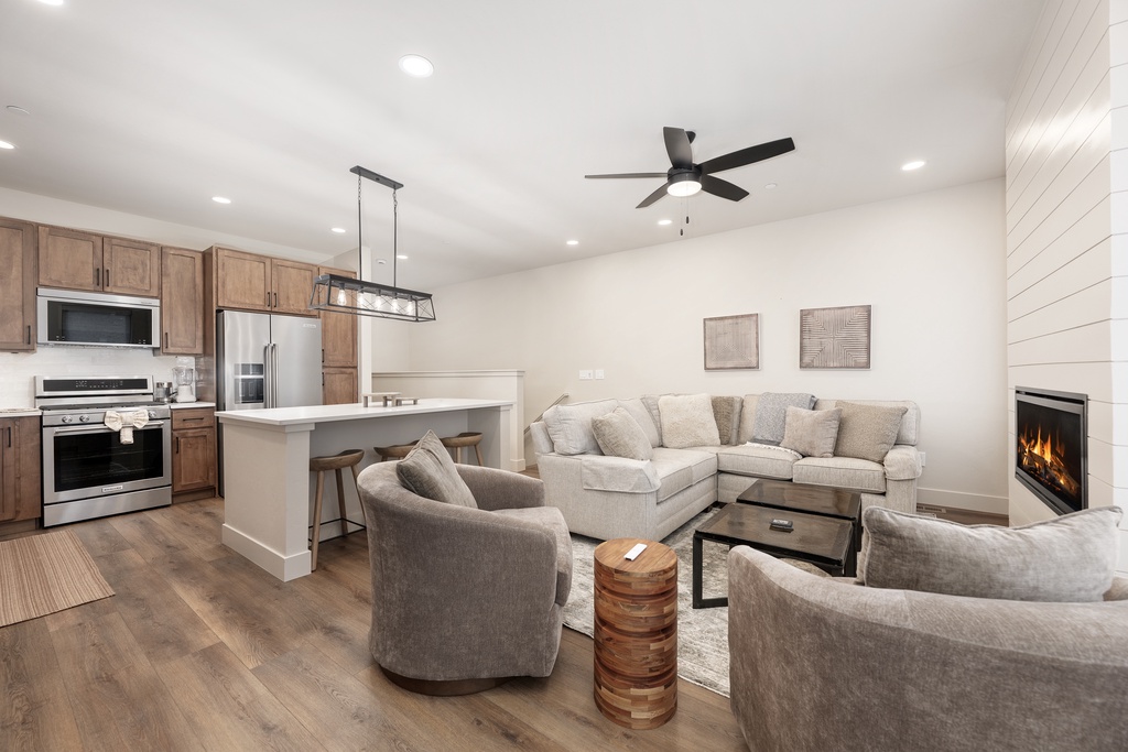 Relax in your spacious open-concept living area featuring plush sectional seating, modern kitchen, and cozy fireplace for perfect evening gatherings.