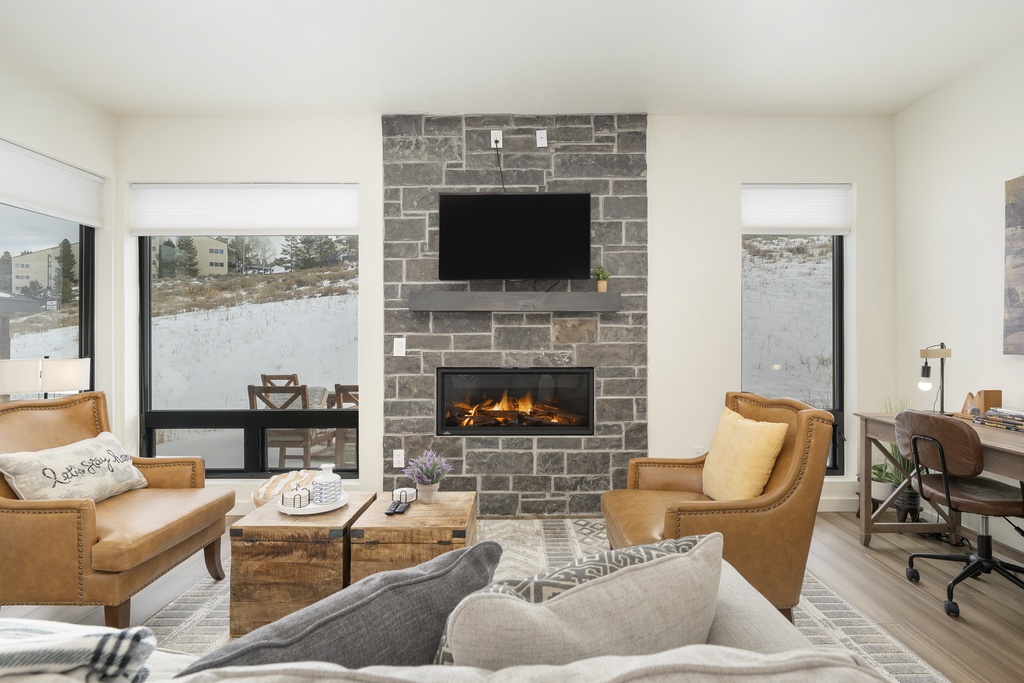 Cozy up by your crackling fireplace in this stylish living room, where leather chairs and panoramic winter views create the perfect retreat.