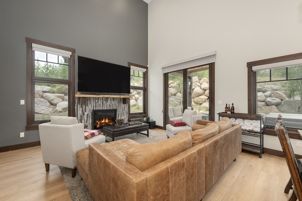 Unwind in your elegant living room featuring a crackling fireplace and luxurious leather seating, while natural boulders frame peaceful views through expansive windows.
