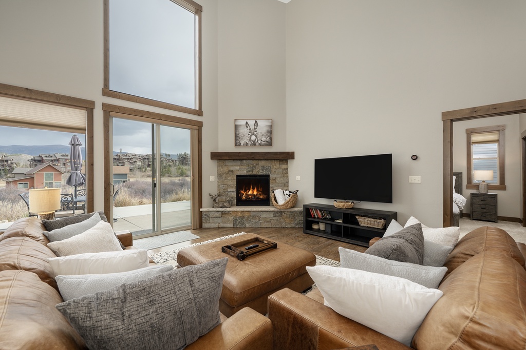 Sink into plush leather sofas beside your crackling stone fireplace, watching sunlight stream through floor-to-ceiling windows in this bright, welcoming living space.