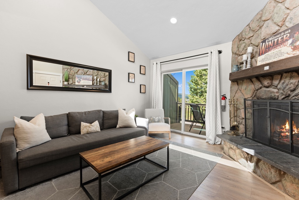 Unwind on the plush sofa by your cozy stone fireplace. Sunlight streams in from the balcony door, and warm tones create a welcoming retreat for your mountain escape.