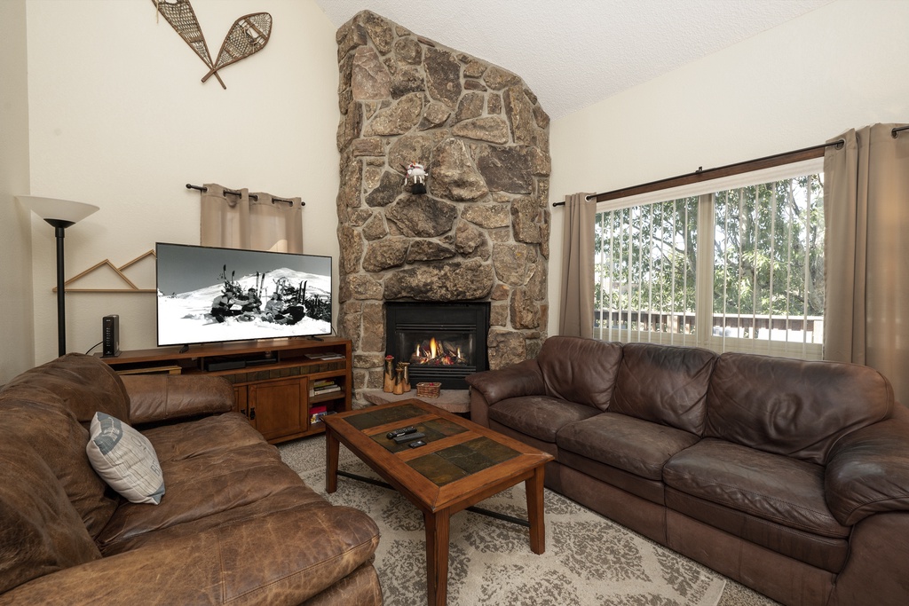 Unwind in your cozy living room with leather seating, stone fireplace, and mountain views through large windows.