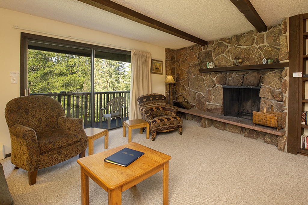 Relax in your cozy living room where exposed beams meet rustic charm, complete with stone fireplace and peaceful forest views from your private balcony.
