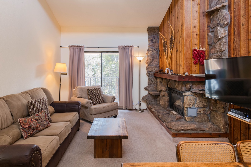 Cozy up by the stone fireplace while you enjoy mountain views from your private balcony in this warm, inviting living space.