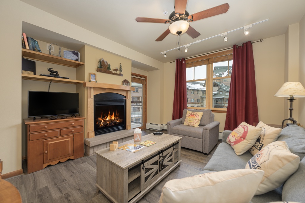 Unwind in your cozy living space with crackling fireplace, plush seating, and mountain views through oversized windows.