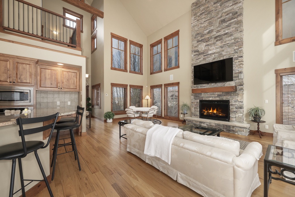 Relax in your spacious living room with soaring ceilings, crackling stone fireplace, and abundant natural light streaming through floor-to-ceiling windows.