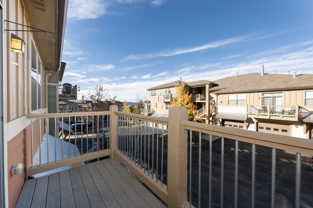 Private balcony offering a quiet residential view surrounded by neighboring homes and autumn trees under a bright sky.