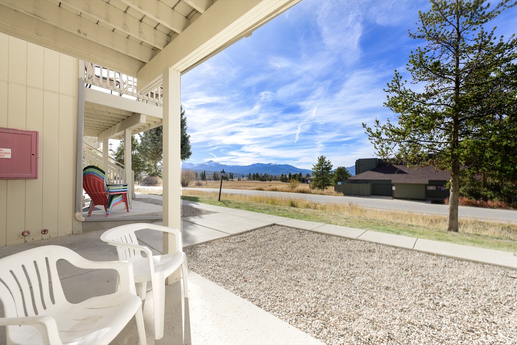 Covered patio with outdoor seating overlooking mountain vistas and open fields in a peaceful residential setting.