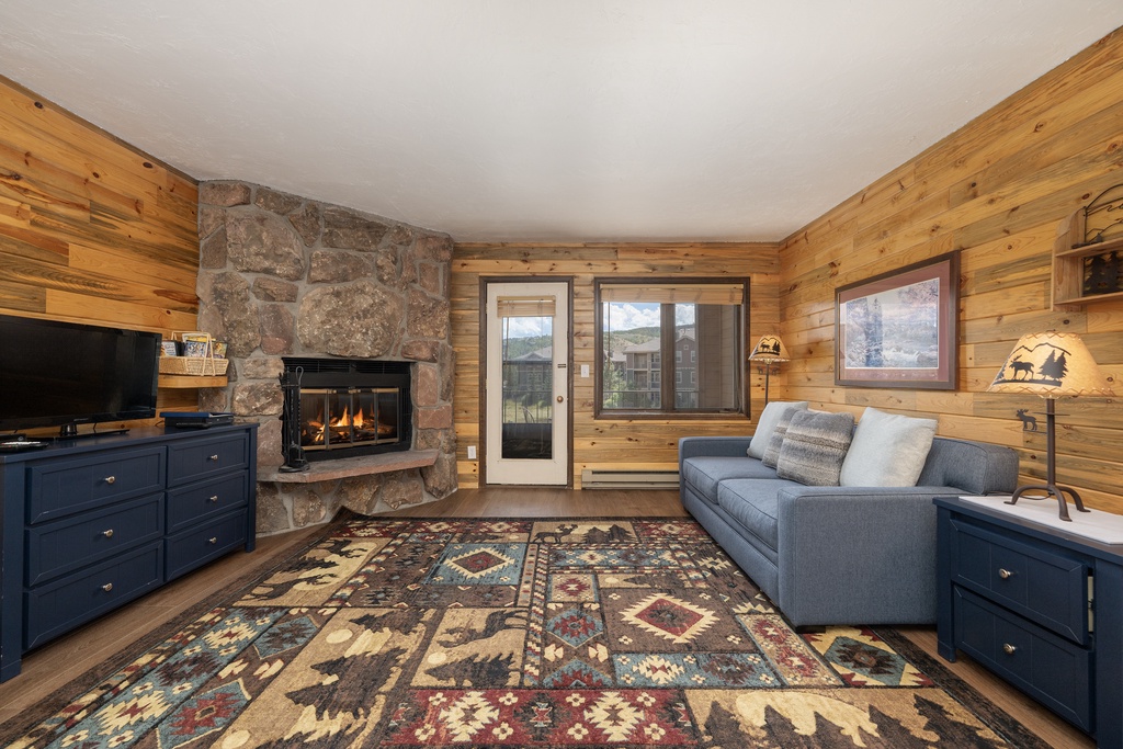Cozy up by your crackling stone fireplace in this warm cabin retreat, where rustic wood walls and comfortable seating create the perfect mountain escape.