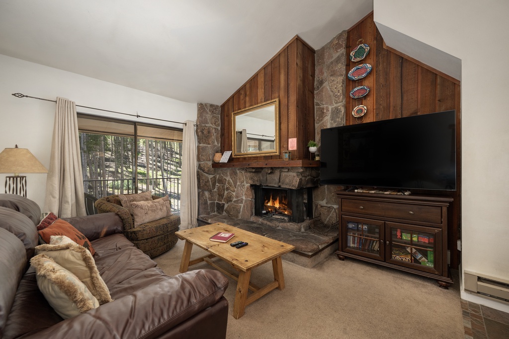 Cozy up in your inviting living room featuring a crackling stone fireplace, plush seating, and mountain views through your private balcony.