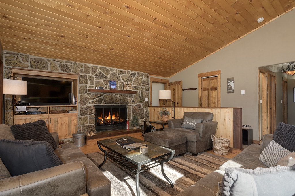 Relax by the crackling stone fireplace in this cozy living room with rustic wood ceilings and plush seating.