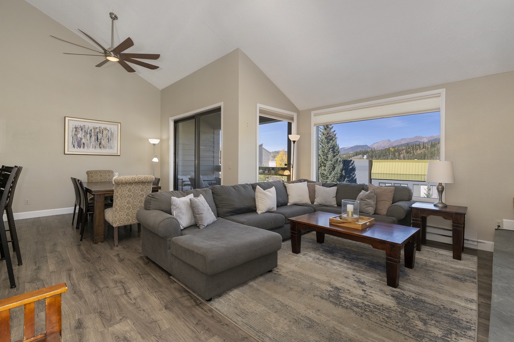 Unwind in your spacious living room with mountain views streaming through large windows, featuring a cozy sectional and modern ceiling fan.