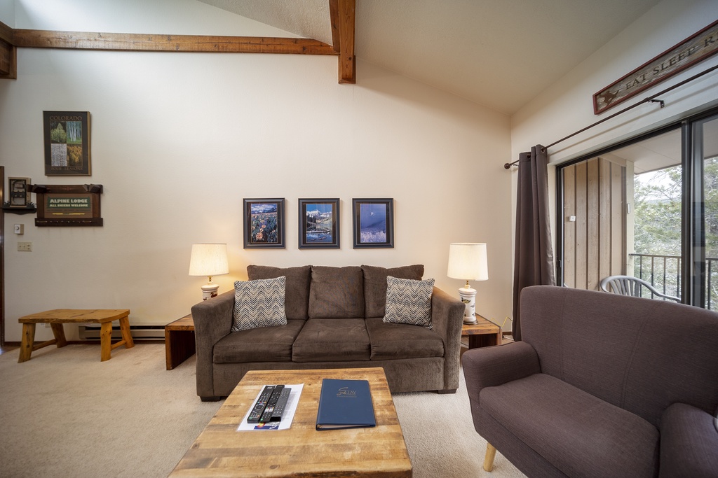 Relax in your cozy living room with exposed wood beams, plush seating, and forest views through the sliding door.
