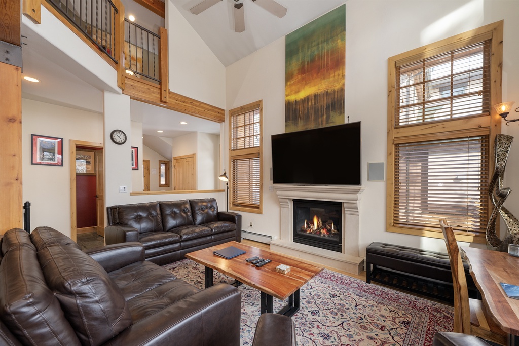 Your spacious living room beckons with plush leather seating, a crackling fireplace, and soaring ceilings that create an airy mountain retreat atmosphere.