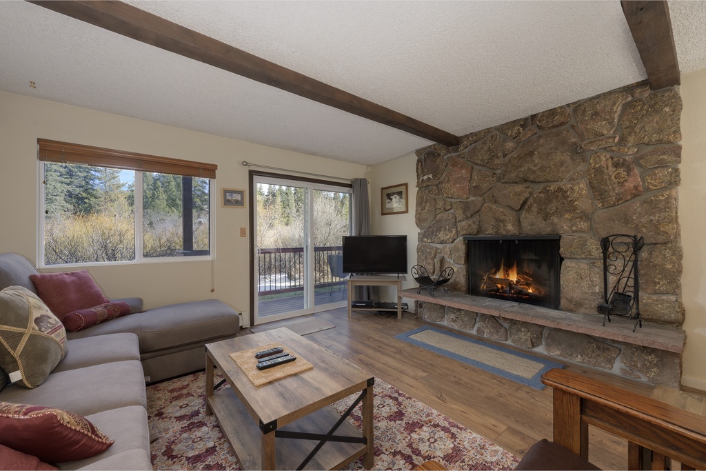 Cozy up by your crackling stone fireplace while enjoying forest views through picture windows in this warm, rustic living space.