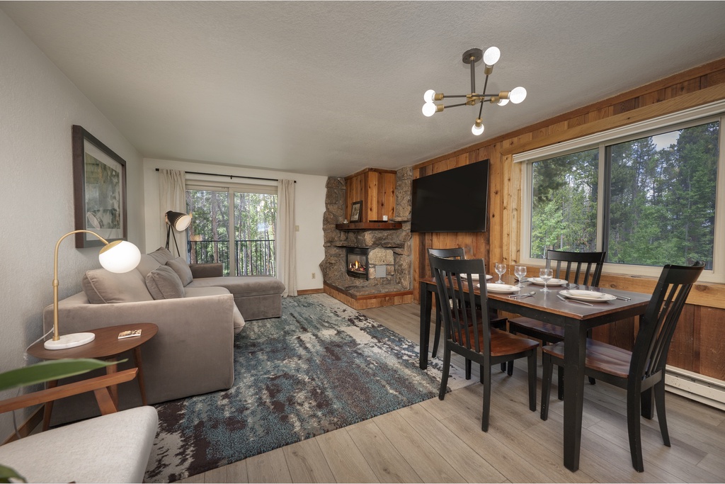 Cozy up by your stone fireplace while enjoying forest views through expansive windows in this warm, wood-accented living space.